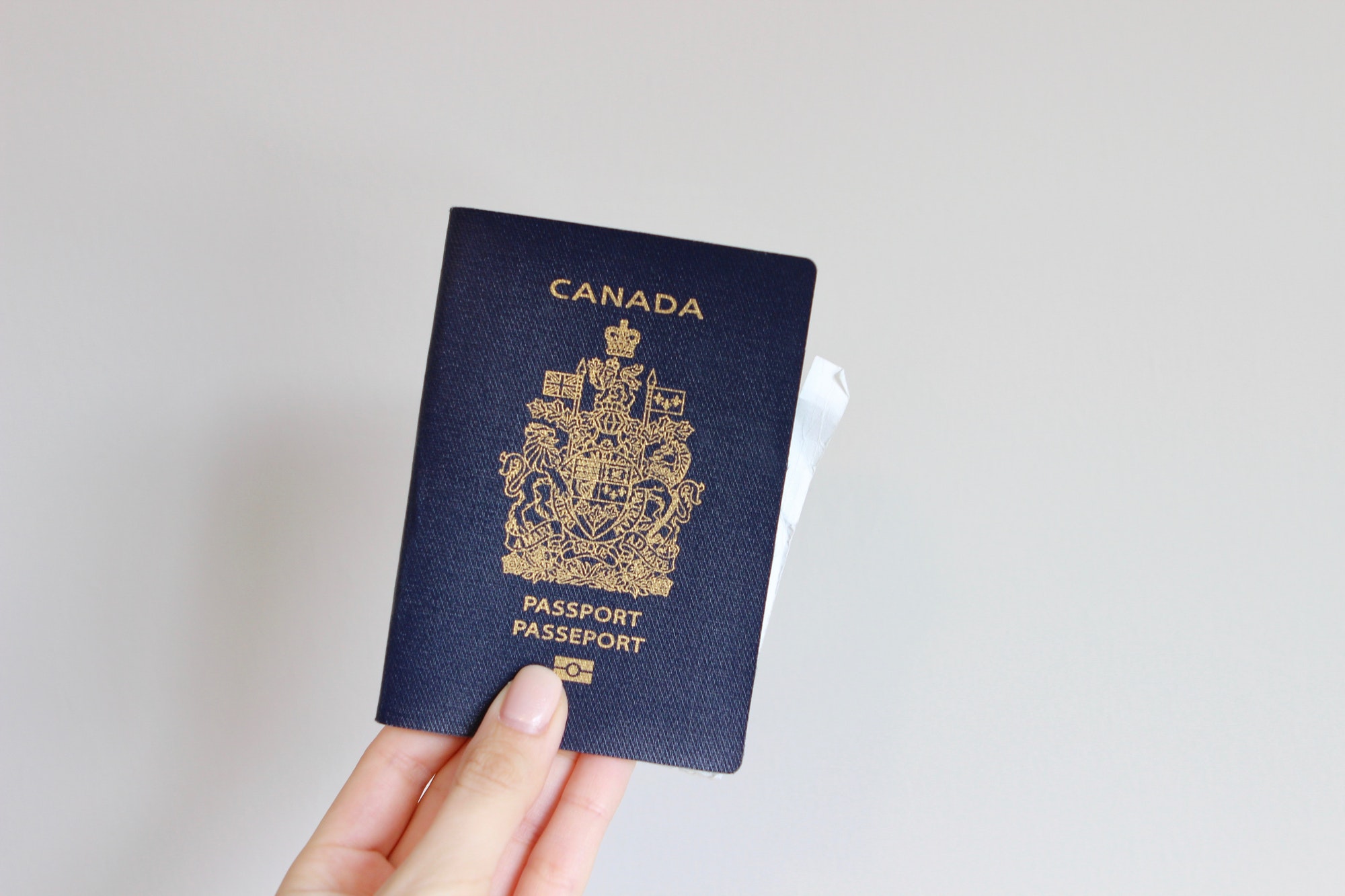 Woman’s hand holding a Canadian passport in front of white background